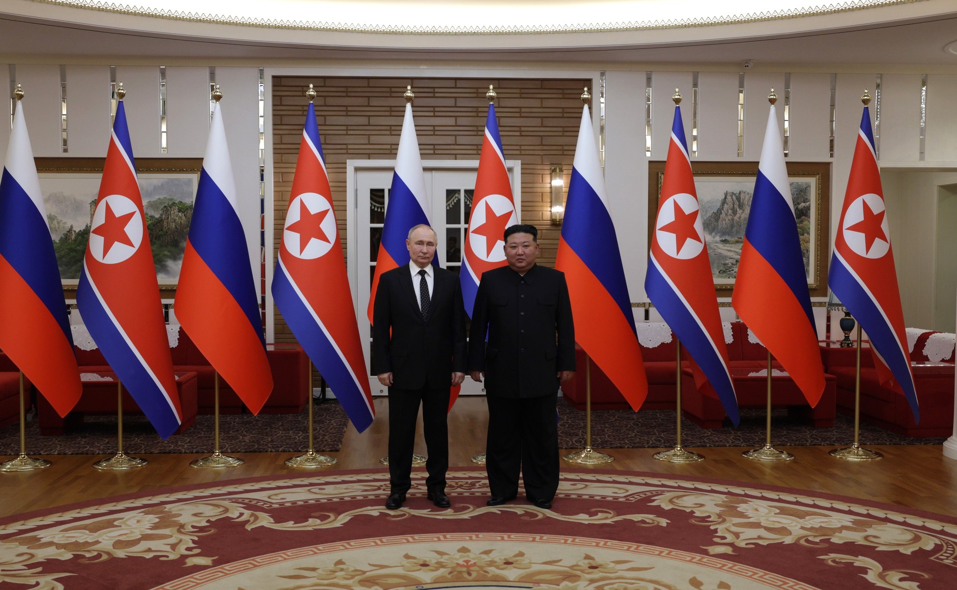 Vladimir Putin and Kim Jong-un standing in front of Russian and North Korean flags in Pyongyang, June 2024