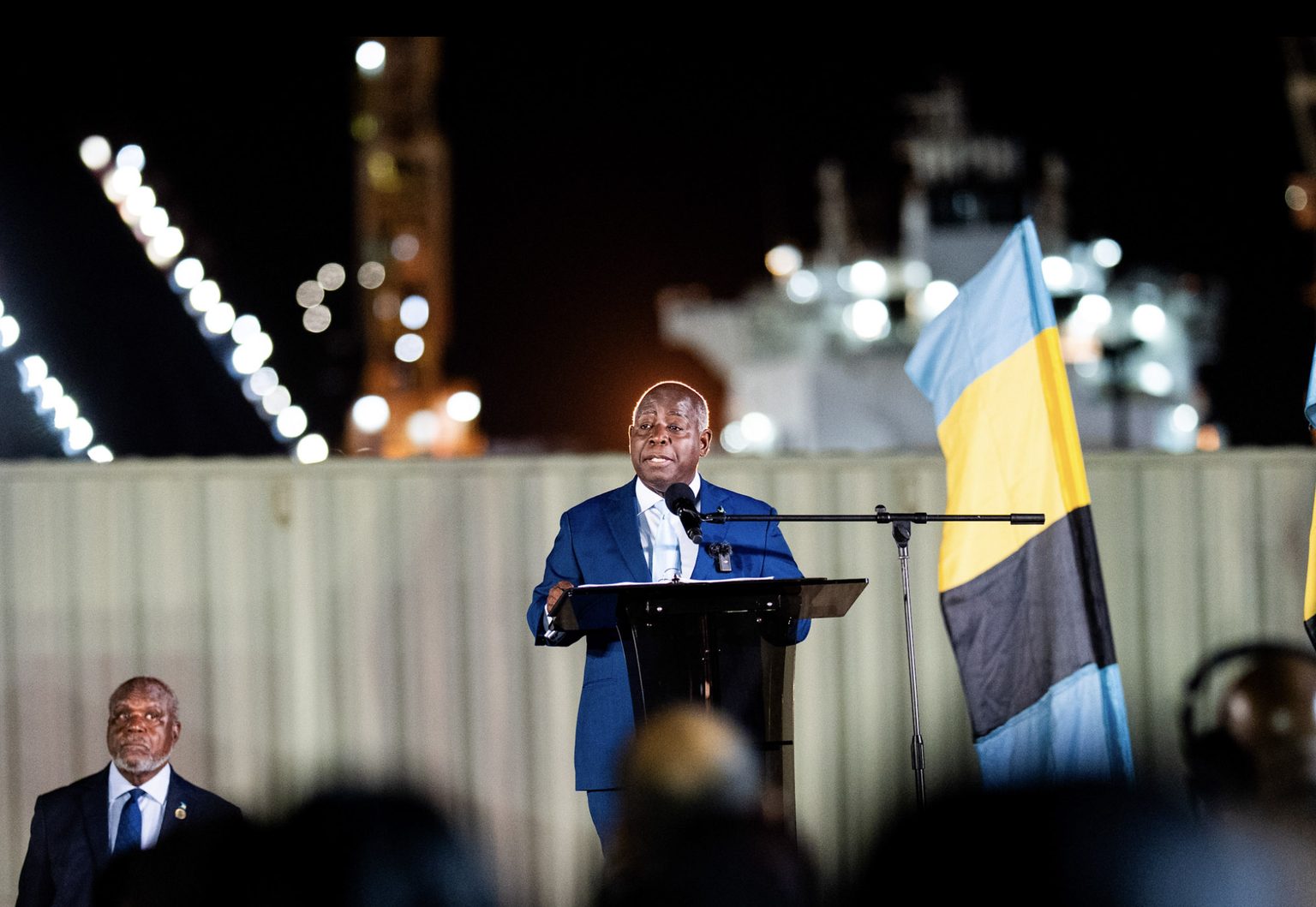 Prime Minister Philip Davis speaking at a podium beside the Bahamian flag at the Grand Bahama Shipyard