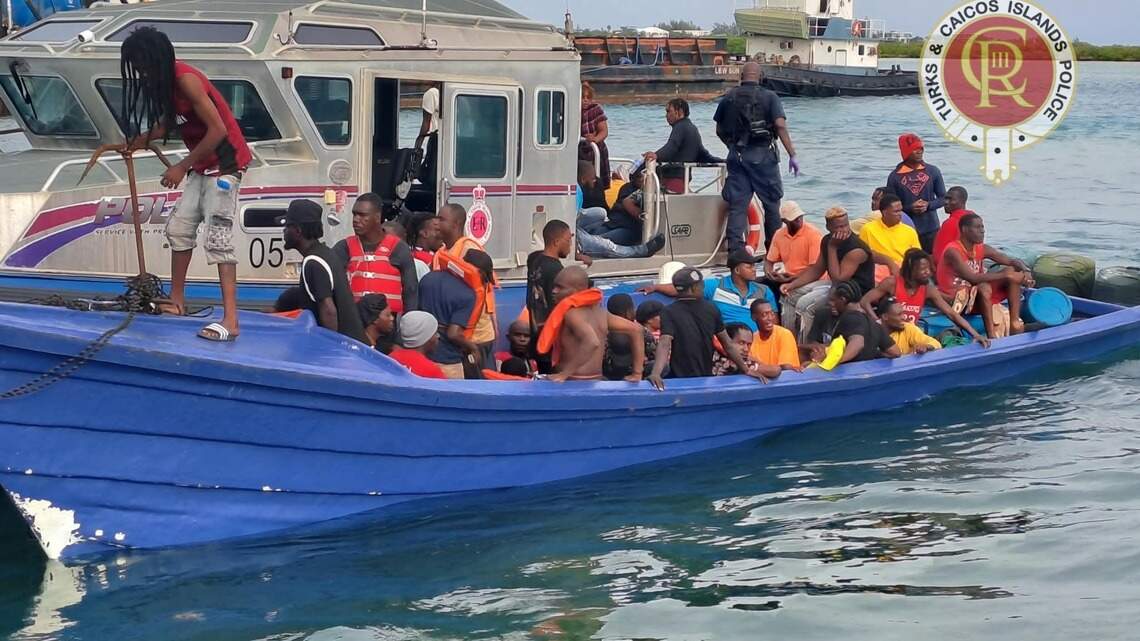 Royal Turks and Caicos Islands Police officers alongside a crowded blue migrant boat